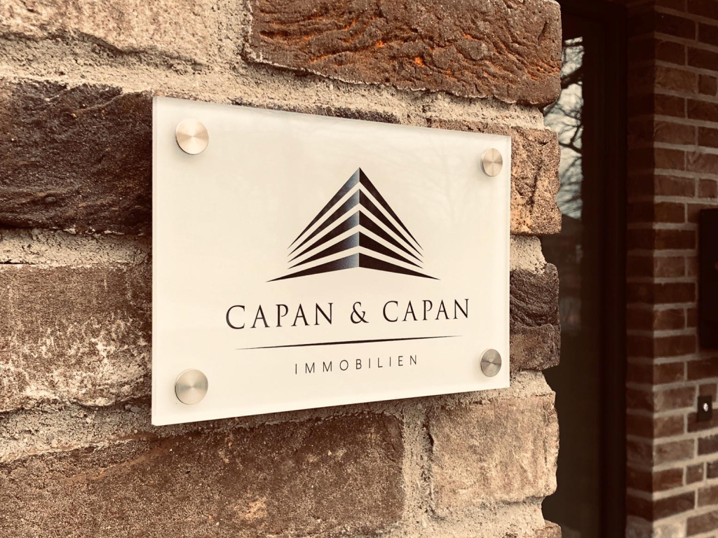 Glasschild mit Capan & Capan Immobilien Logo im Innenbereich.